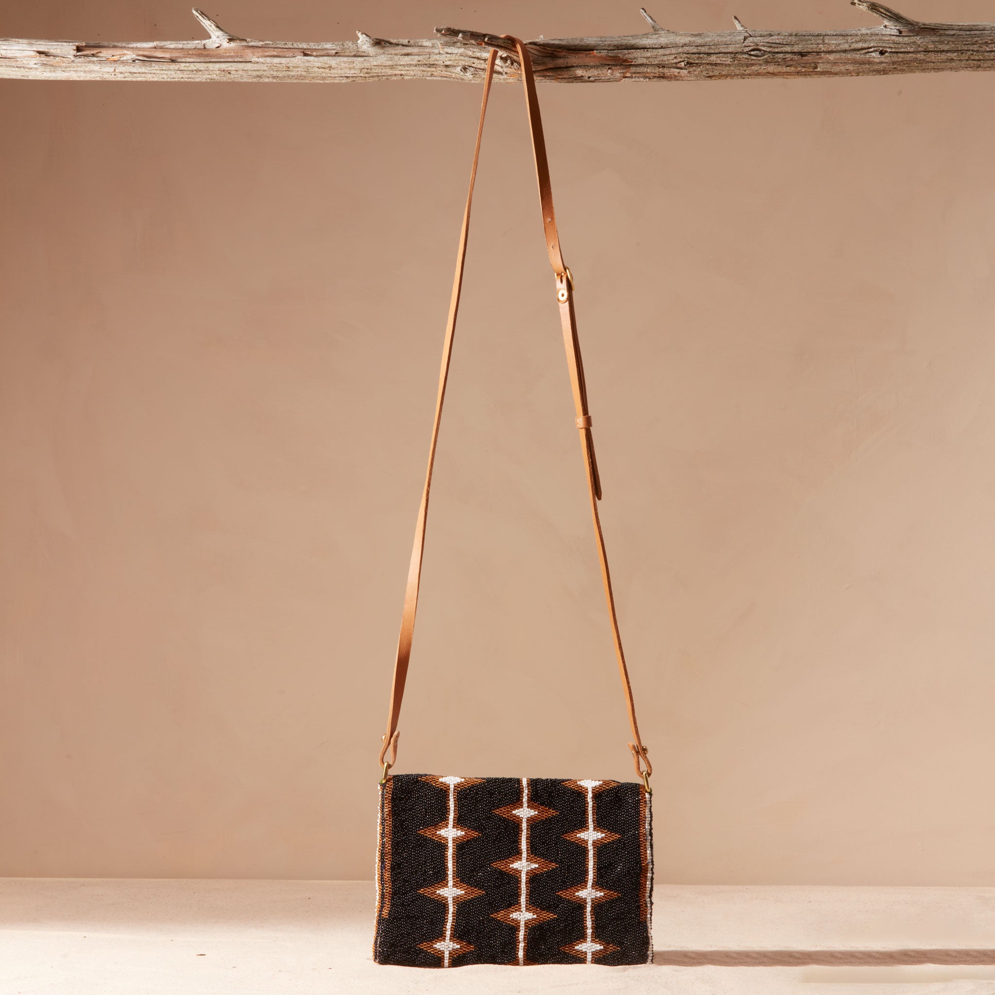 Back view of beaded handbag with a brown leather strap hanging on a branch