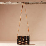 Beaded handbag with a brown leather strap hanging on a branch