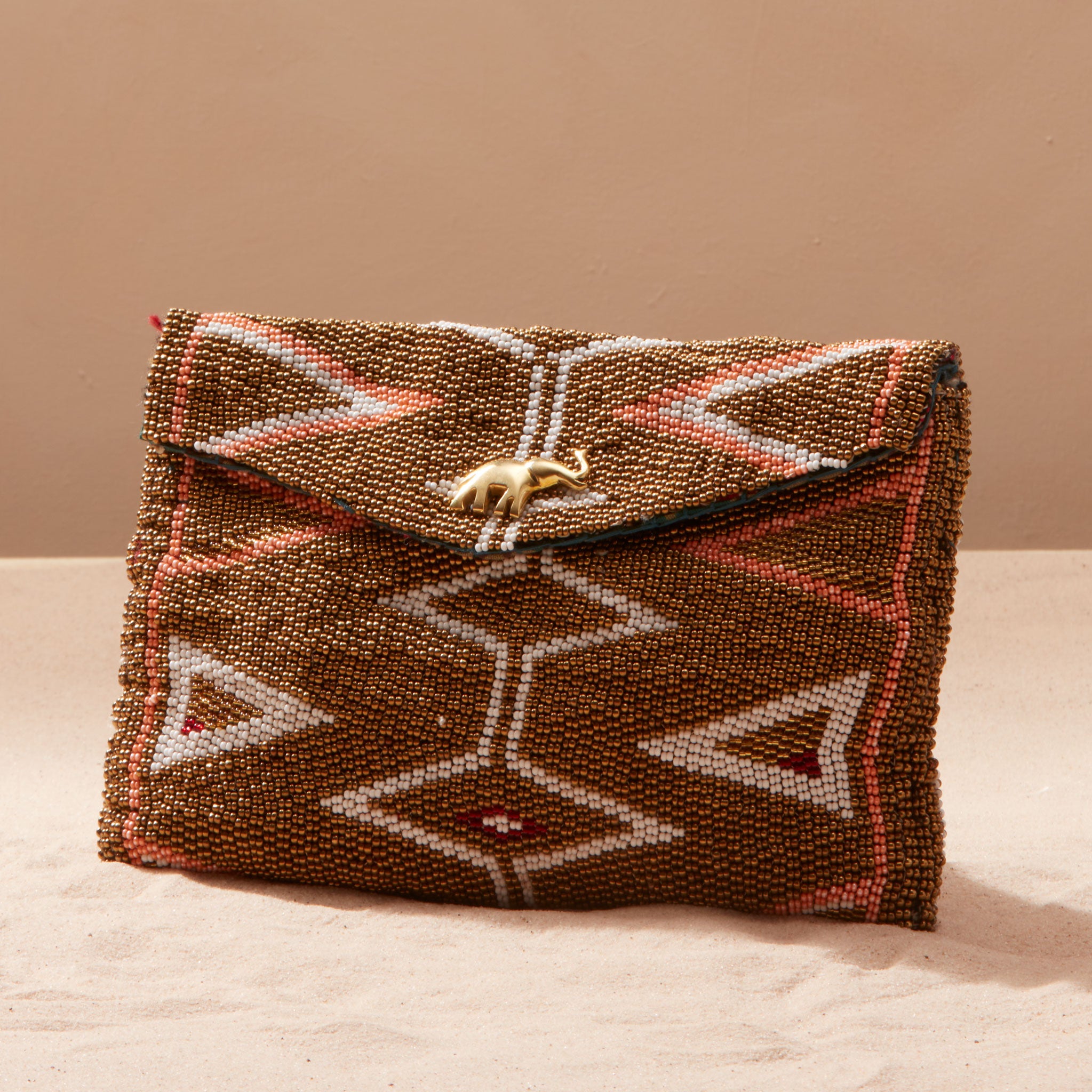 Beaded clutch with geometric pattern and a brass elephant on a sand background