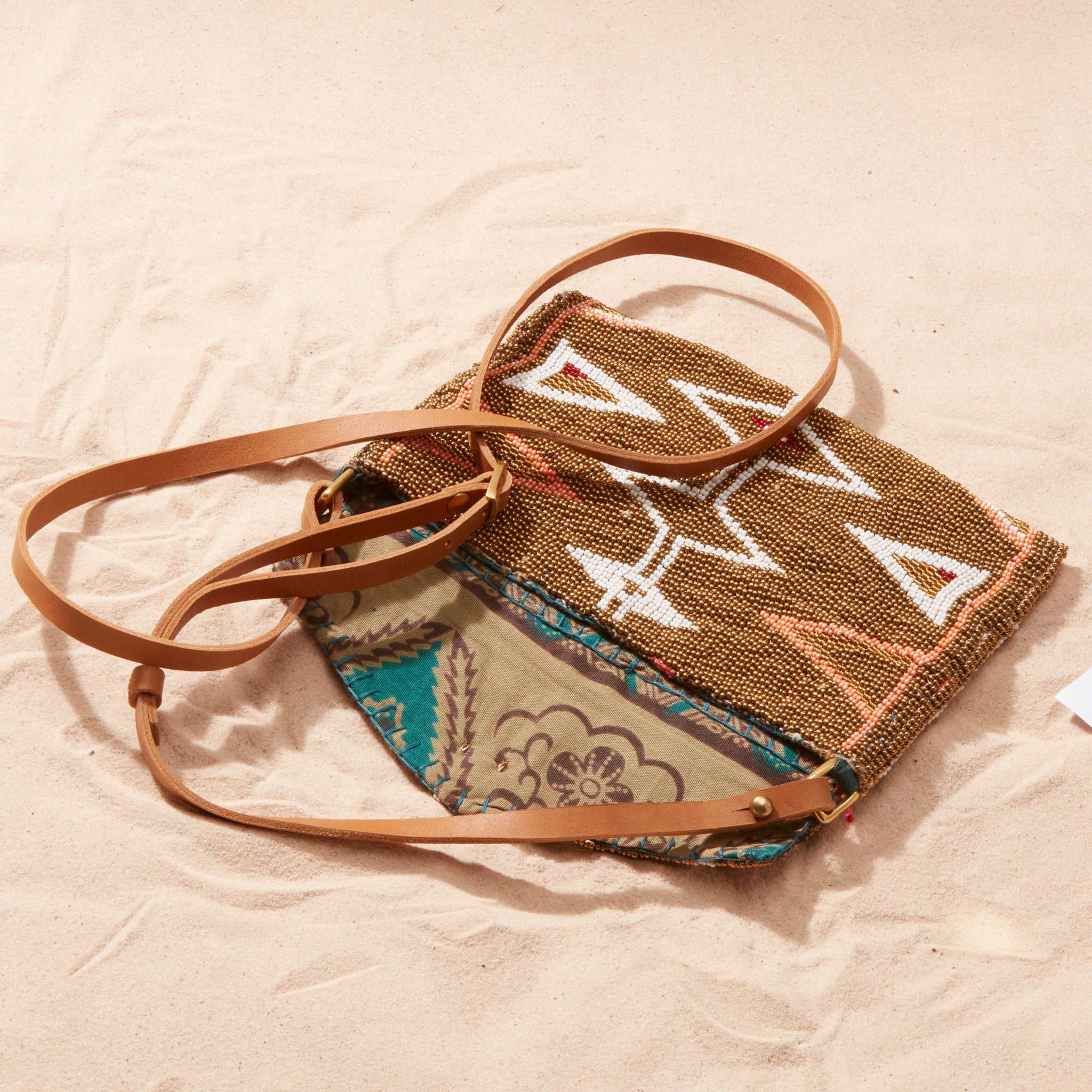 Beaded bag with brown leather strap open showing colorful kanga fabric lining