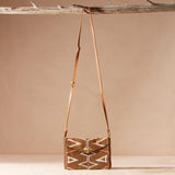 Beaded handbag with geometric pattern and a brown leather strap hanging on a branch