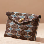 Beaded clutch bag with geometric pattern and brass elephant on a sand background