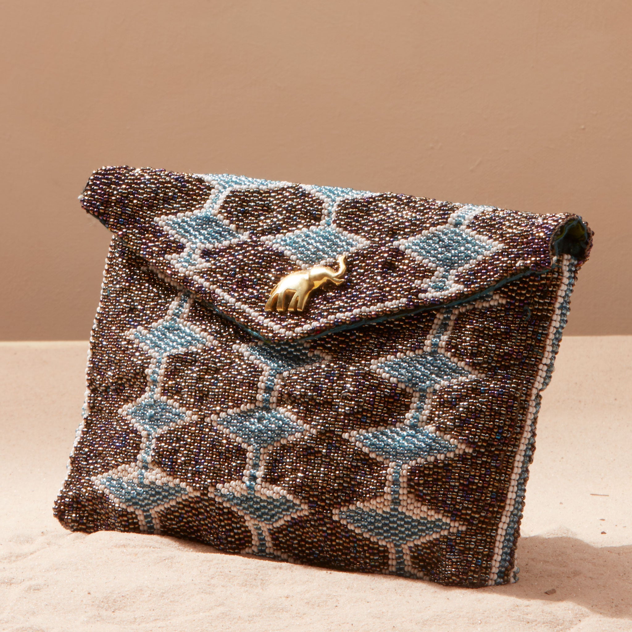 Beaded clutch bag with geometric pattern and brass elephant on a sand background