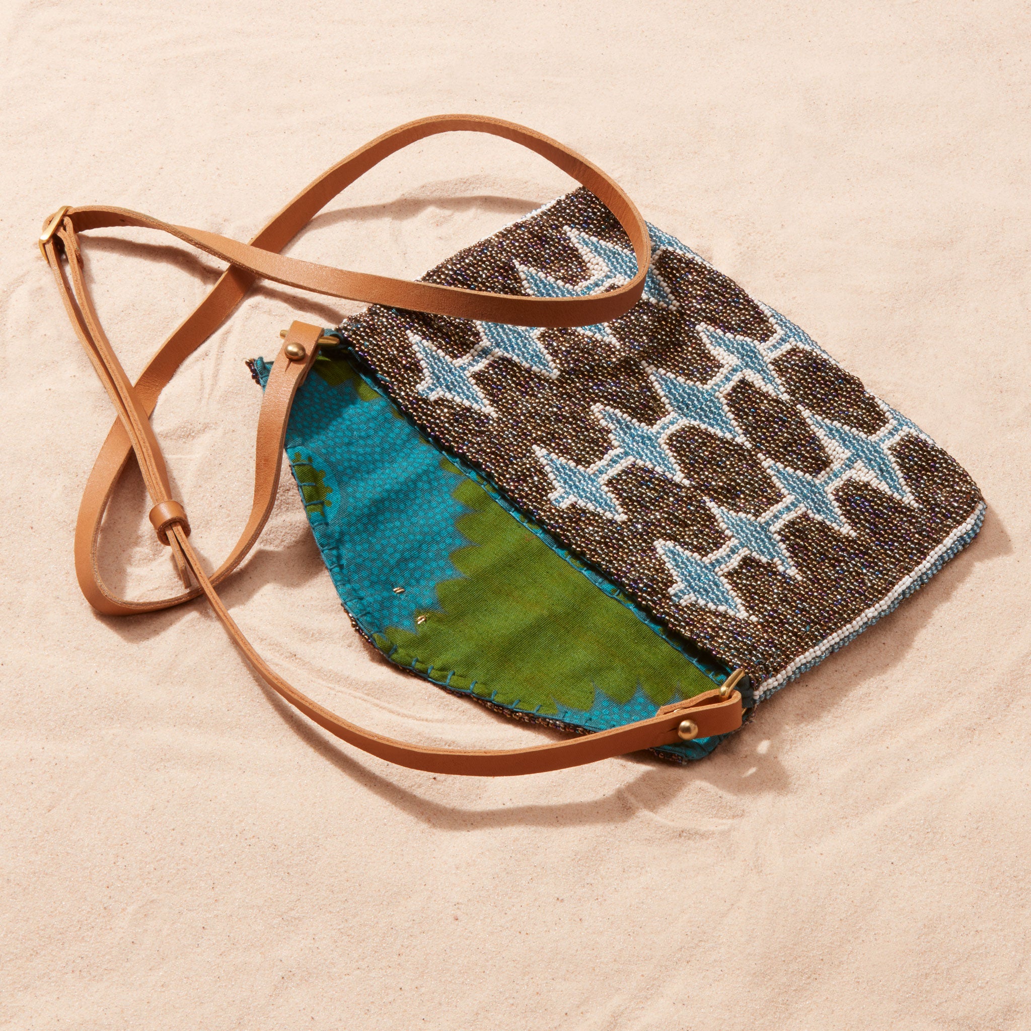 Handbag with a geometric pattern and brown leather strap open showing a colorful kanga lining