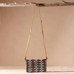 Handbag with a geometric pattern and a brown leather strap hanging on a branch