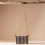 Handbag with a geometric pattern and a brown leather strap hanging on a branch