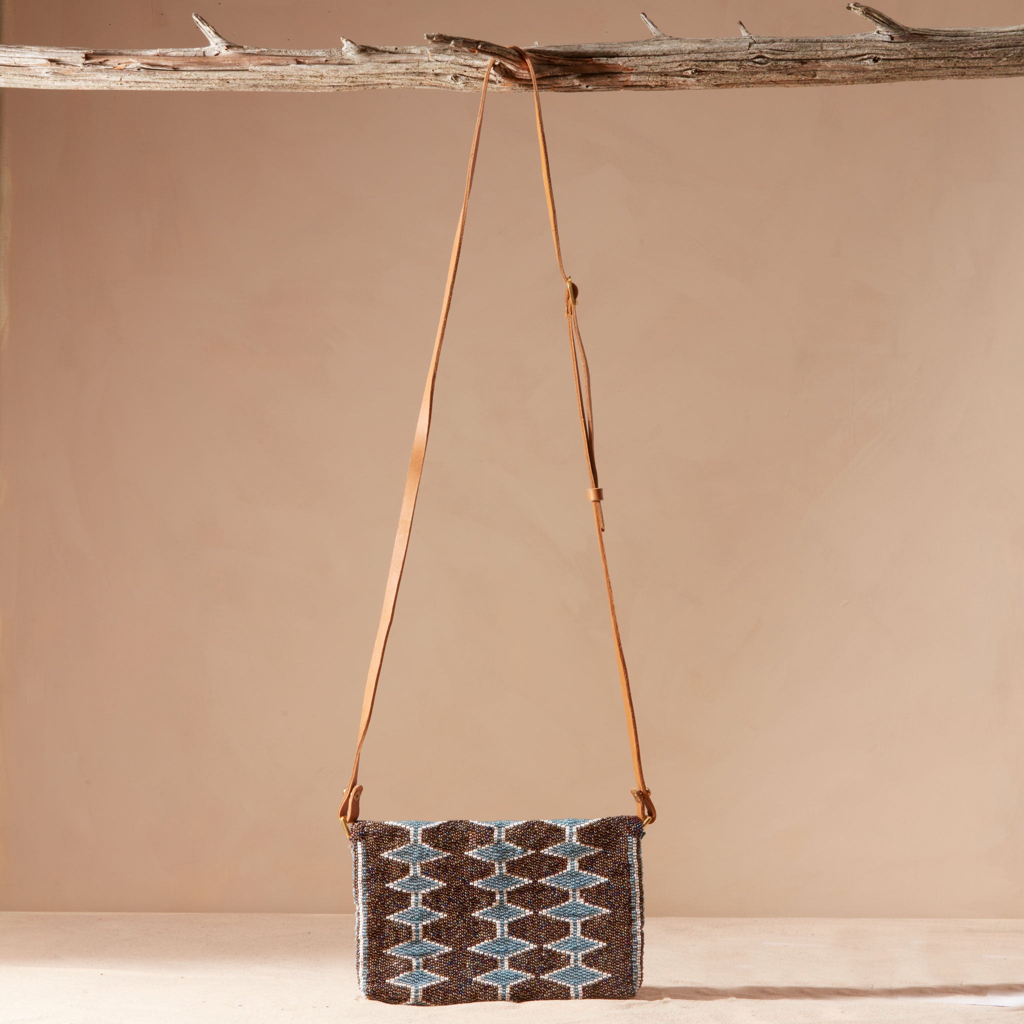 Handbag with a geometric pattern and a brown leather strap hanging on a branch