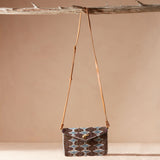 Beaded handbag with a geometric pattern hanging on a branch against a beige background