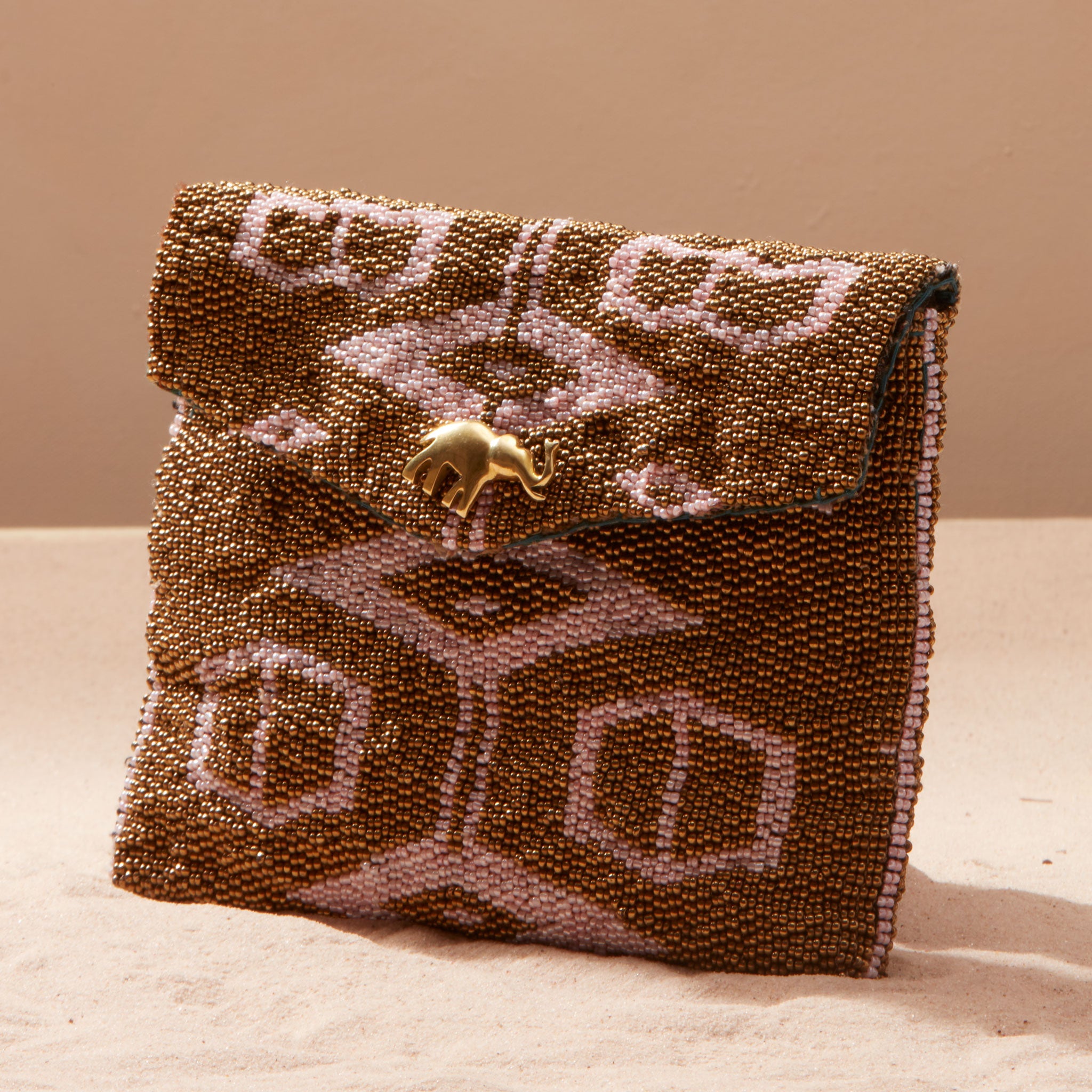 Beaded clutch bag with intricate pattern and brass elephant on a sand background