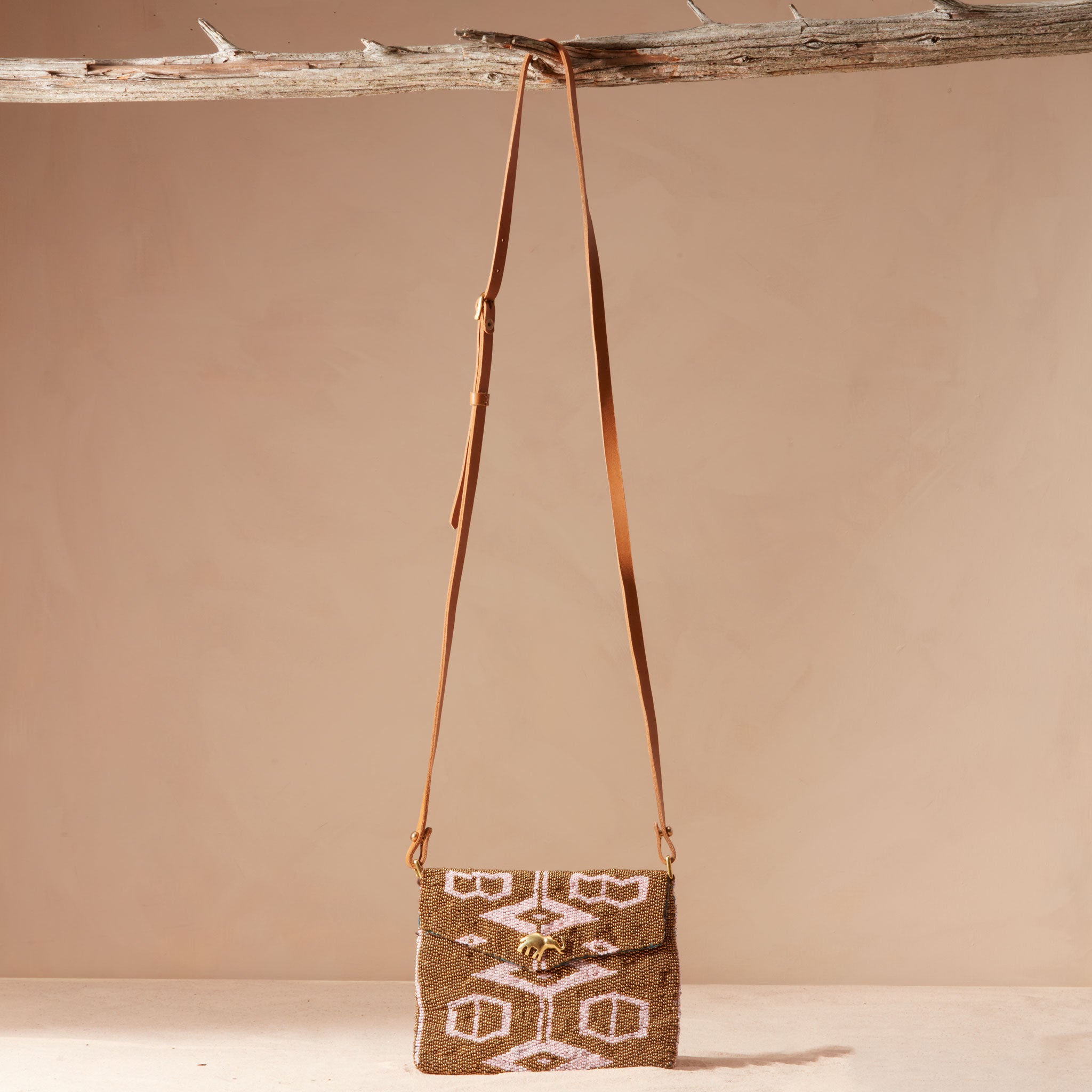 Gold and pink beaded handbag with a leather strap hanging on a branch