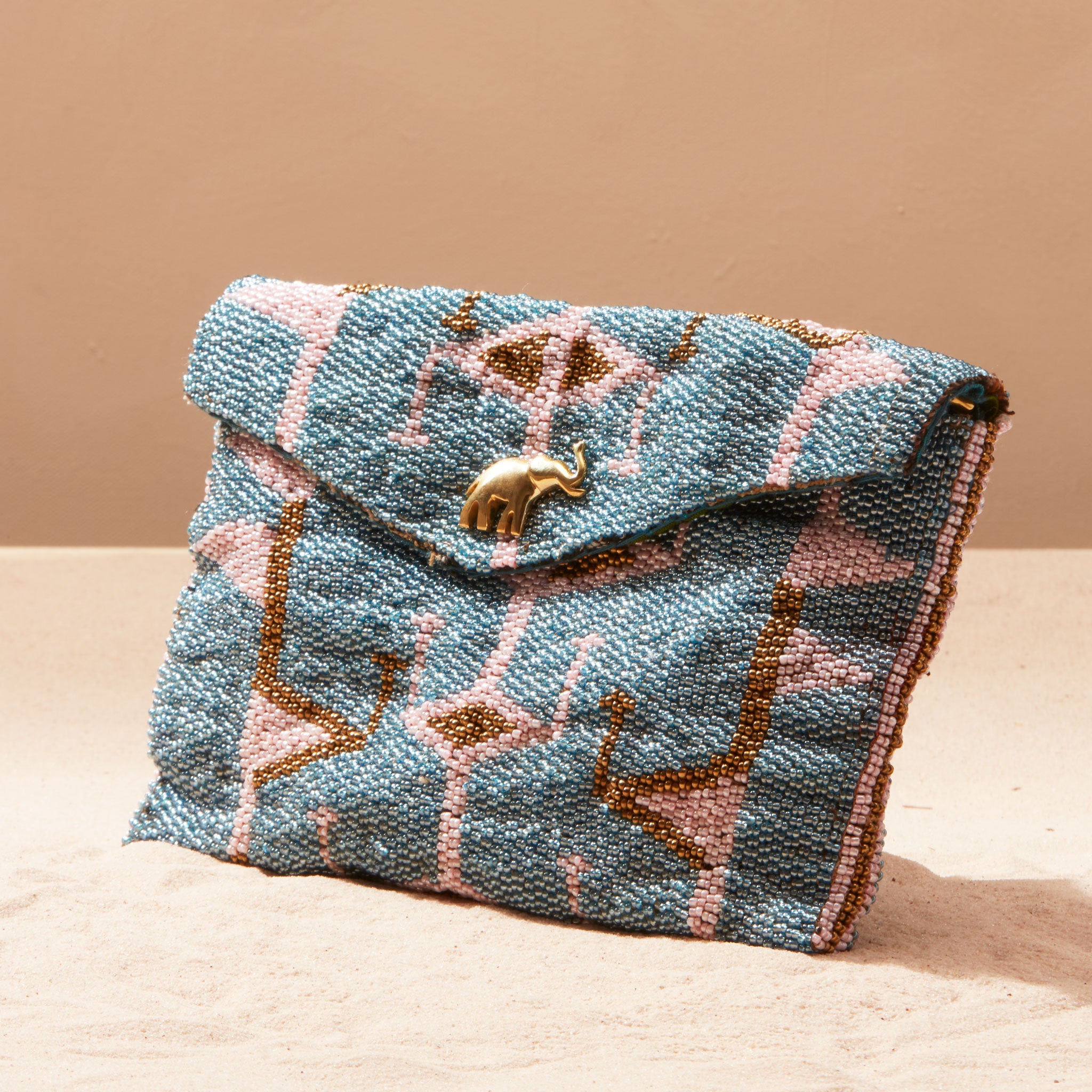 Beaded blue and pink handbag with gold accents on a sand surface