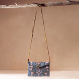 Beaded bag in a geometric pattern with a brown leather strap hanging on a branch