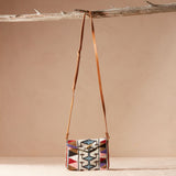 Multicolored patterned handbag with brown leather strap hanging on a branch