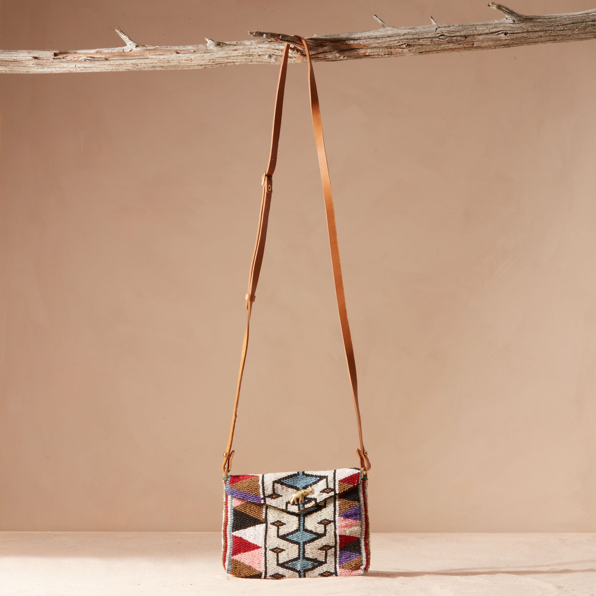 Multicolored patterned handbag with brown leather strap hanging on a branch