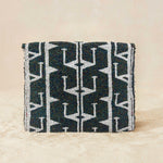 Back view of a small beaded clutch bag with a iridescent dark grey and white geometric pattern and a small gold elephant charm on the front, photographed against a beige background.