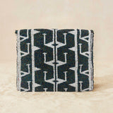 Back view of a small beaded clutch bag with a iridescent dark grey and white geometric pattern and a small gold elephant charm on the front, photographed against a beige background.