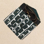 Interior view of a small beaded clutch bag with a iridescent dark grey and white geometric pattern, featuring a green, mint and brown kanga fabric interior and a brown leather crossbody strap, photographed against a beige background.