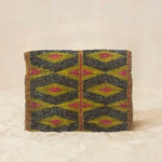 Back view of small beaded clutch bag with a geometric pattern in iridescent bronze and blue with a yellow and pink geometric pattern, featuring a small gold elephant charm on the front flap, set against a neutral beige background.