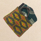 Interior view of a small beaded clutch bag with a geometric pattern in iridescent bronze and blue with a yellow and pink geometric pattern, featuring green, mint and brown kanga fabric lining and a brown leather crossbody strap, set against a neutral beige background.