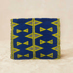 Back view of small beaded clutch bag with a blue and yellow geometric pattern, featuring a small elephant charm on the front flap, set against a neutral beige background.