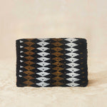 Back view of small beaded rectangular clutch bag with a black, brown, and white geometric diamond pattern and a small gold elephant charm on the front flap, set against a neutral beige background.