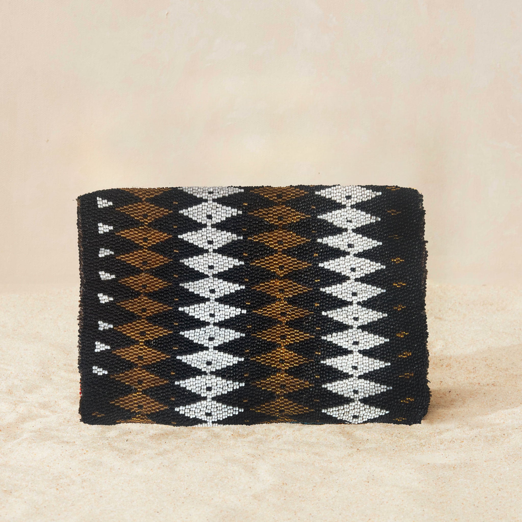 Back view of small beaded rectangular clutch bag with a black, brown, and white geometric diamond pattern and a small gold elephant charm on the front flap, set against a neutral beige background.