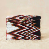 A beaded clutch purse featuring a bold chevron pattern in black, white, red, and brown, with a small gold elephant charm on the front flap, on a neutral beige background.