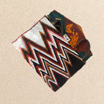 Interior view of beaded clutch purse featuring a bold chevron pattern in black, white, red, and brown, featuring colorful orange and green kanga fabric lining and a brown leather strap, on a neutral beige background.