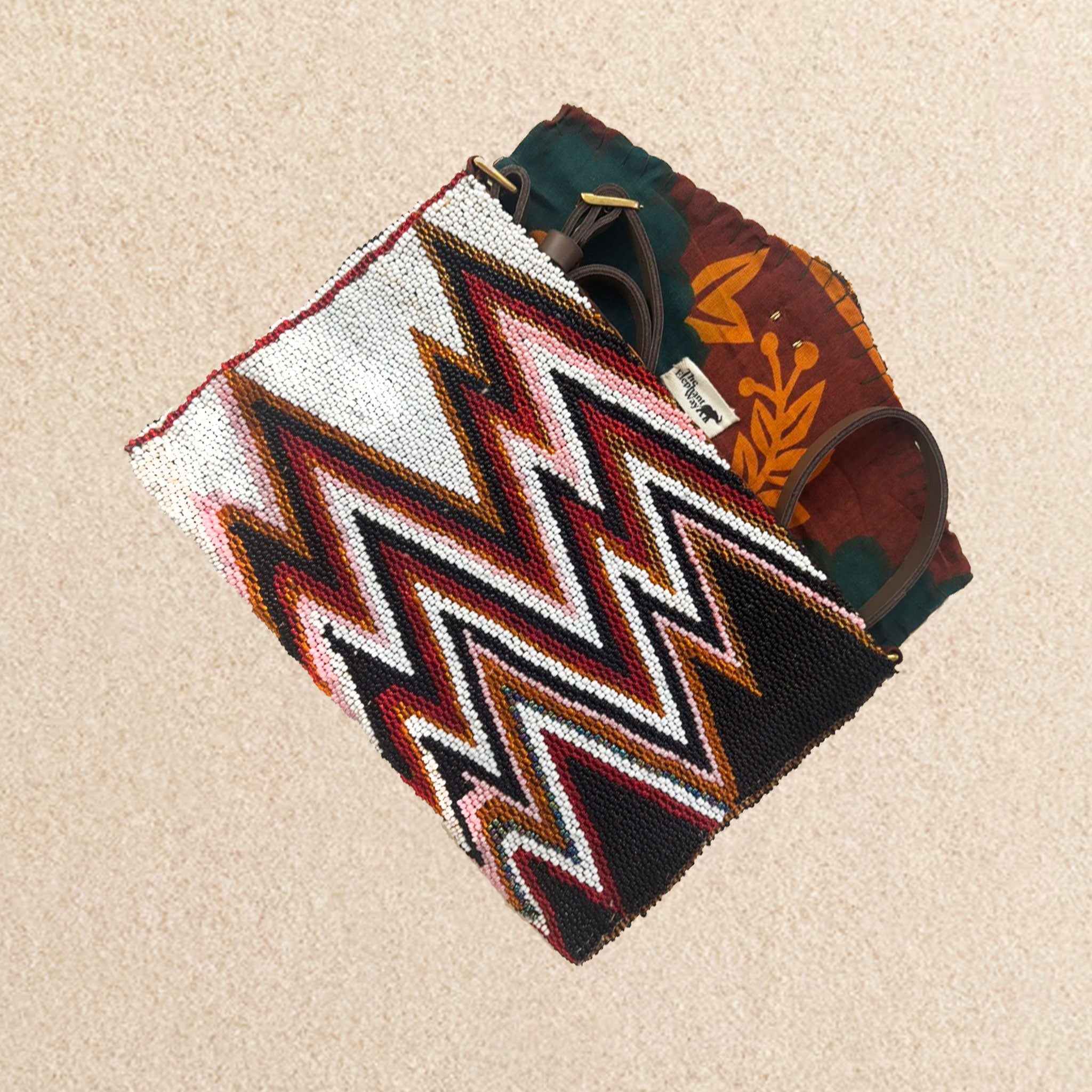 Interior view of beaded clutch purse featuring a bold chevron pattern in black, white, red, and brown, featuring colorful orange and green kanga fabric lining and a brown leather strap, on a neutral beige background.