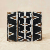 Back view of small beaded clutch bag with a geometric pattern in black, brown, and white, featuring a small gold elephant clasp on the front flap, set against a neutral beige background.