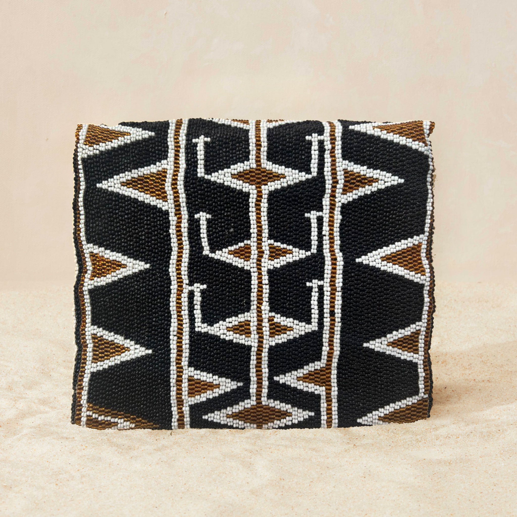 Back view of small beaded clutch bag with a geometric pattern in black, brown, and white, featuring a small gold elephant clasp on the front flap, set against a neutral beige background.
