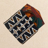 Interior view of a small beaded clutch bag with a geometric pattern in black, brown, and white, featuring a colorful orange, green kanga fabric lining and brown leather crossbody strap, set against a neutral beige background.