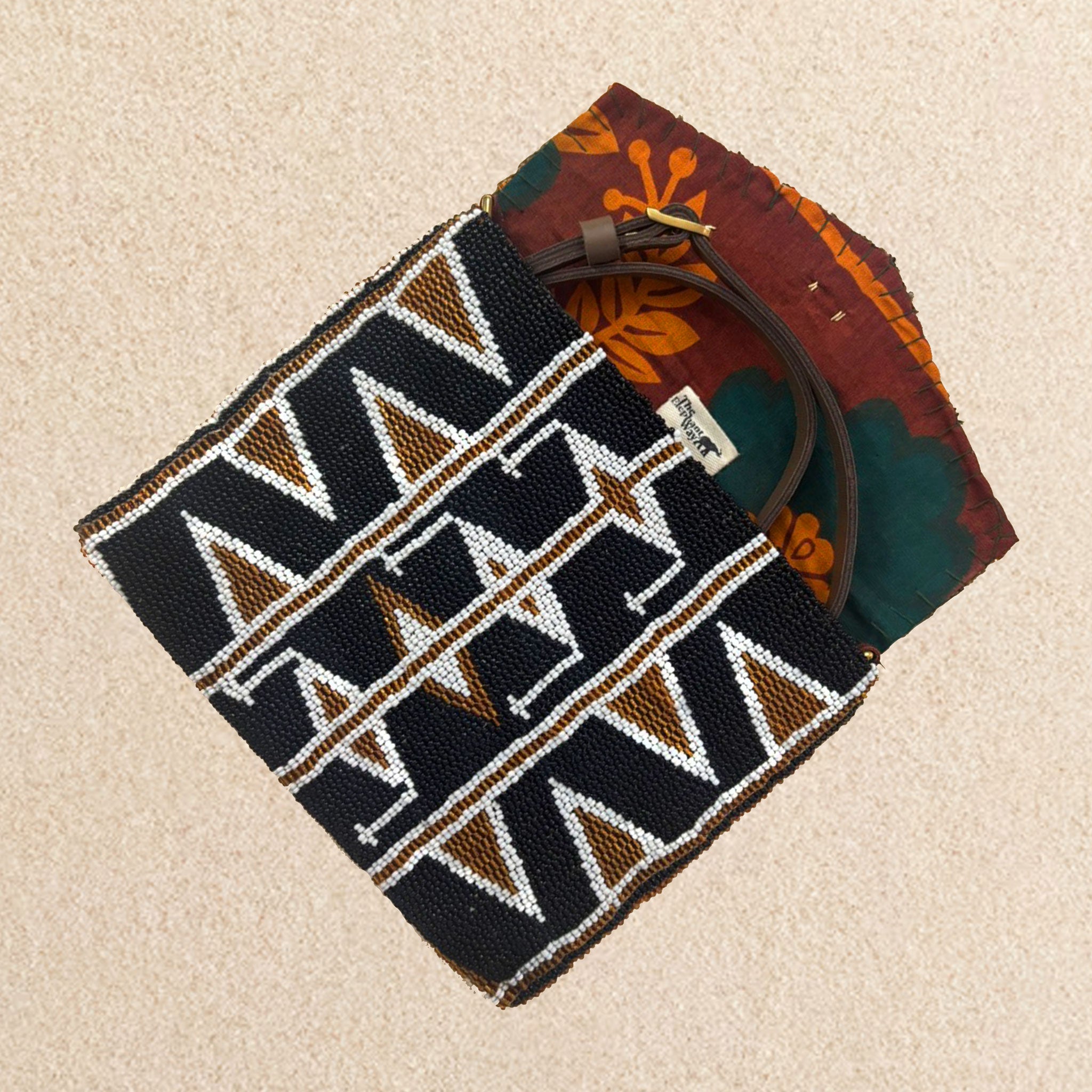 Interior view of a small beaded clutch bag with a geometric pattern in black, brown, and white, featuring a colorful orange, green kanga fabric lining and brown leather crossbody strap, set against a neutral beige background.
