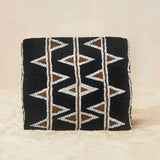 Back view of black beaded clutch purse featuring a geometric pattern of white, bronze and red triangles, with a small gold elephant charm on the front flap, set against a neutral beige background.