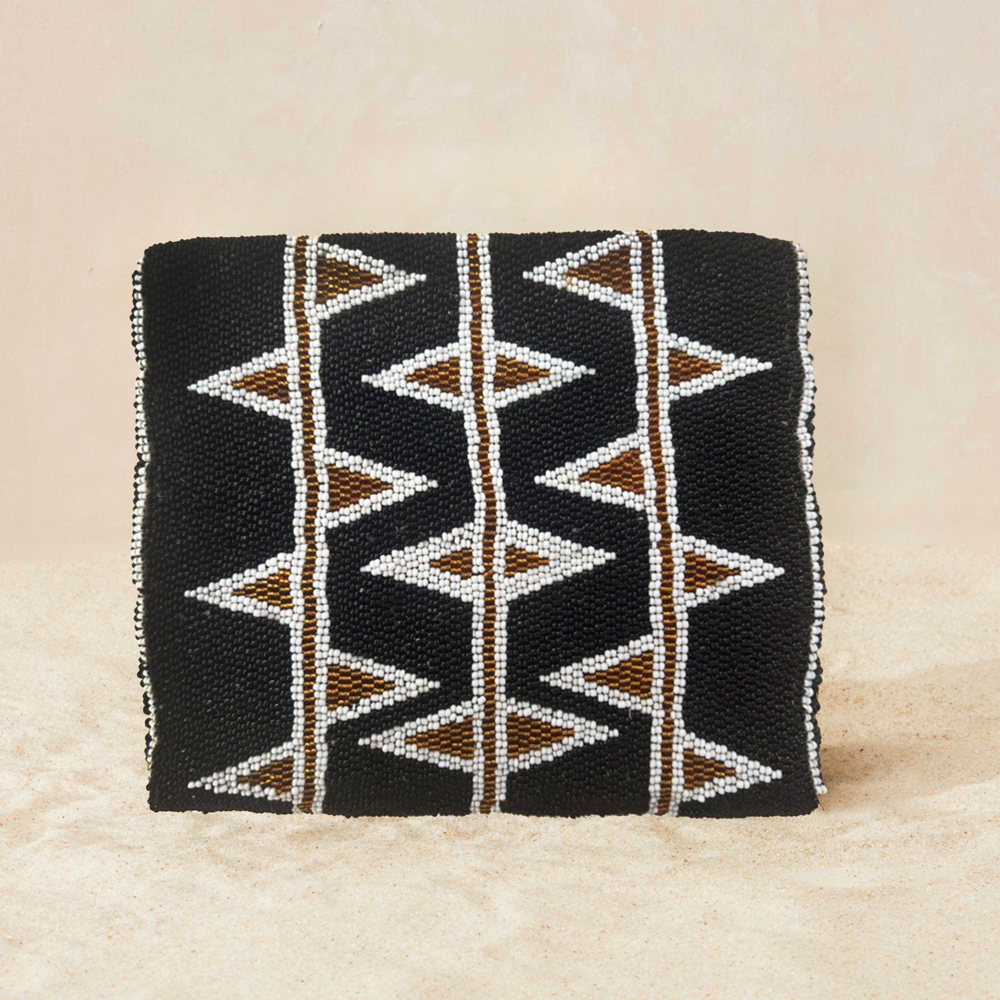 Back view of black beaded clutch purse featuring a geometric pattern of white, bronze and red triangles, with a small gold elephant charm on the front flap, set against a neutral beige background.
