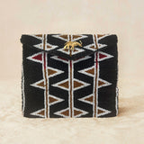 A black beaded clutch purse featuring a geometric pattern of white, bronze and red triangles, with a small gold elephant charm on the front flap, set against a neutral beige background.