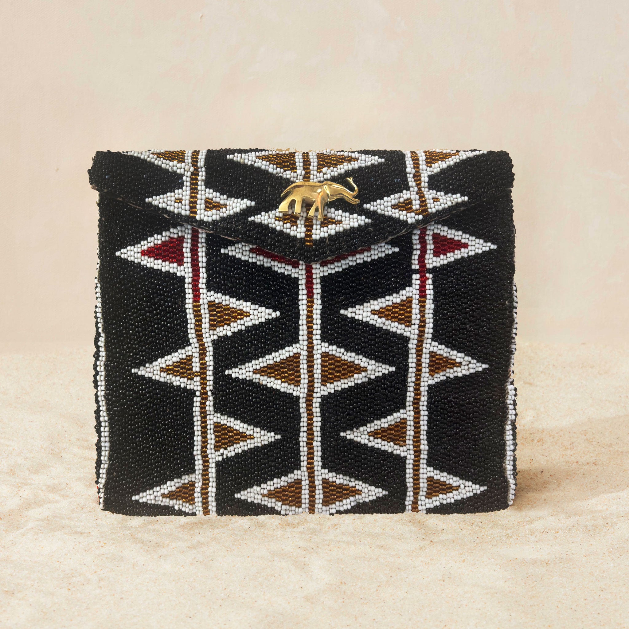 A black beaded clutch purse featuring a geometric pattern of white, bronze and red triangles, with a small gold elephant charm on the front flap, set against a neutral beige background.