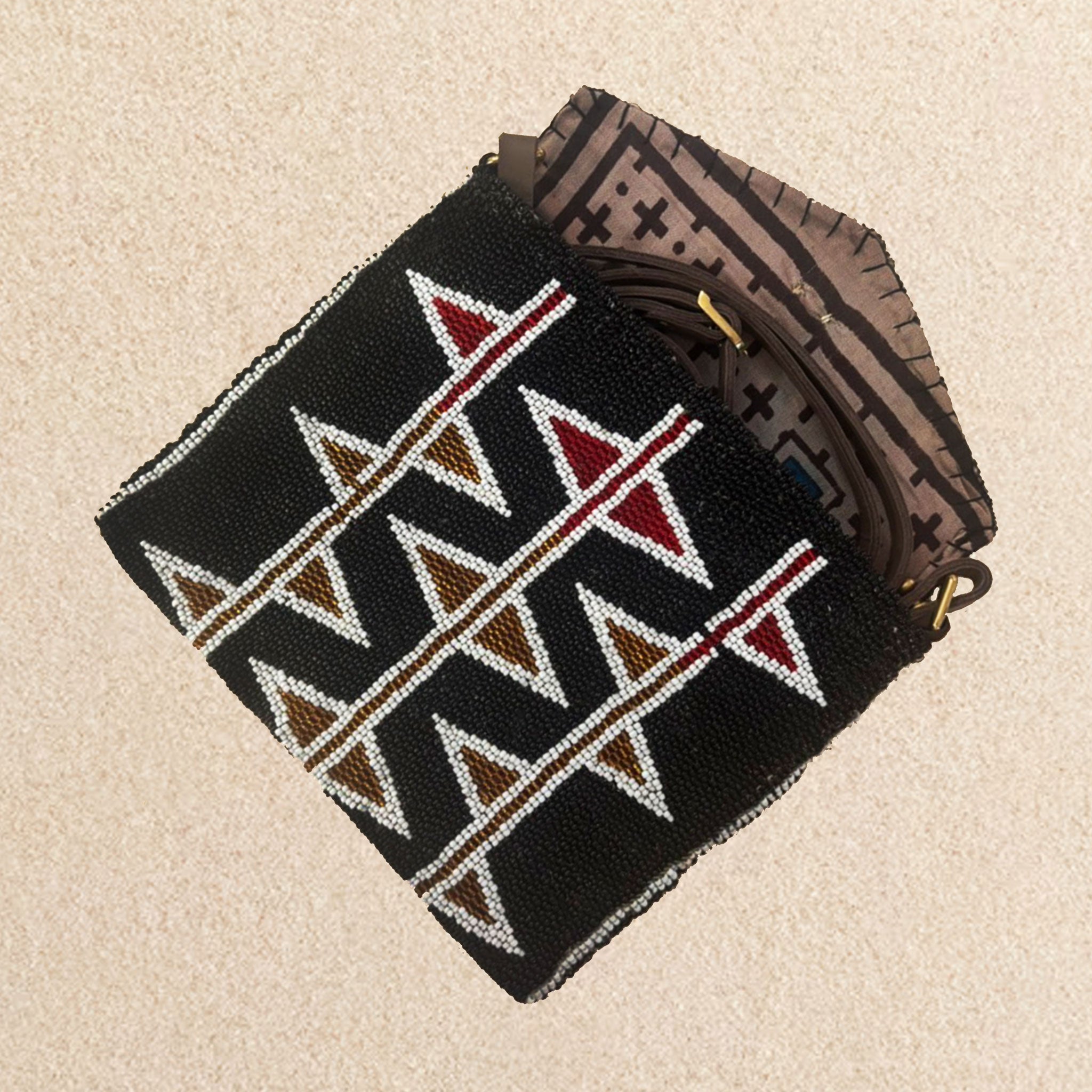 Interior view  of black beaded clutch purse featuring a geometric pattern of white, bronze and red triangles, showing a neutral kanga fabric lining and brown leather crossbody strap, set against a neutral beige background.