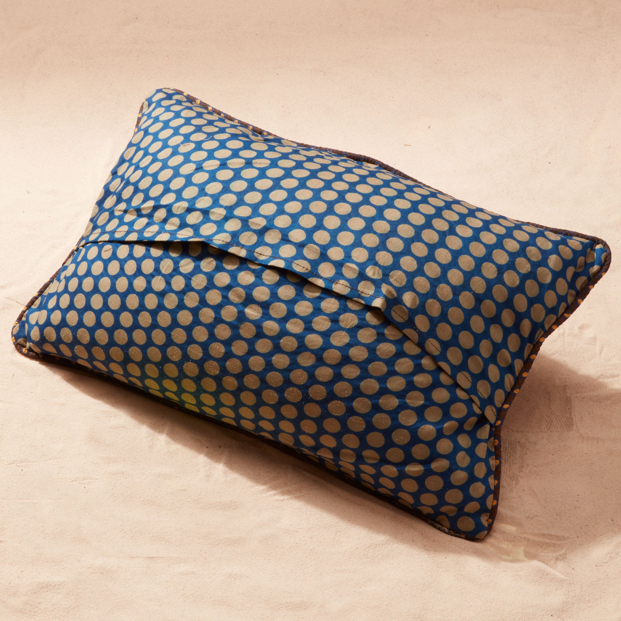 Back of pillow showing blue and beige polka dot fabric on a beige background
