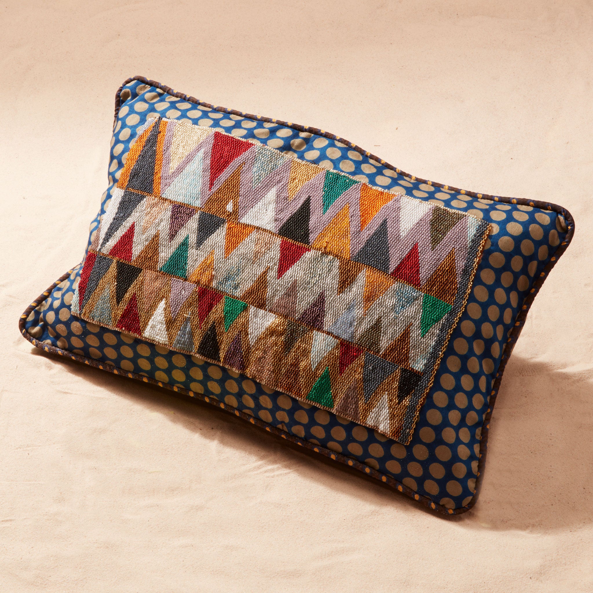Decorative pillow with beaded geometric pattern on a sand background