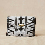 Black and white patterned beaded clutch bag with a brass elephant on a beige background