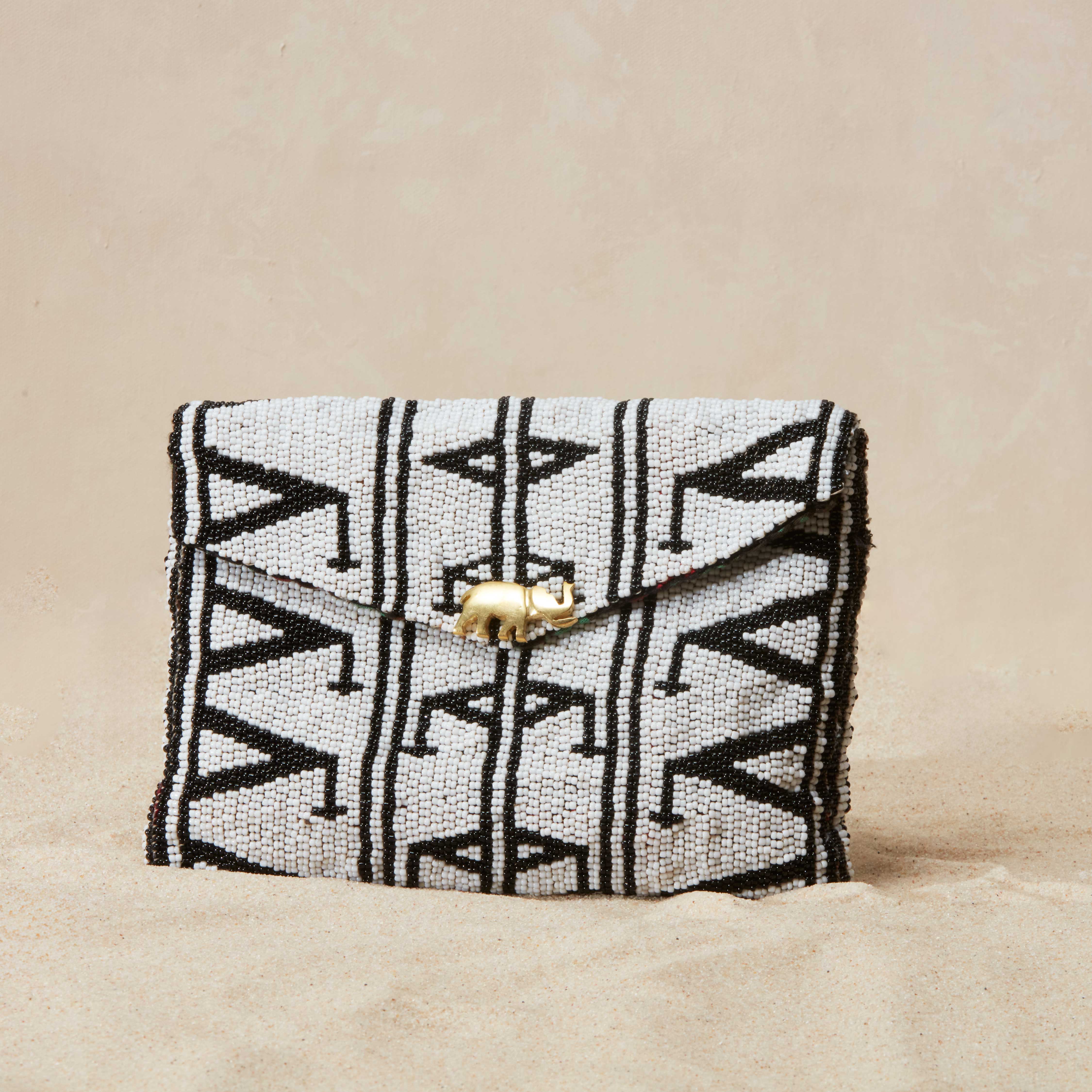 Black and white patterned beaded clutch bag with a brass elephant on a beige background