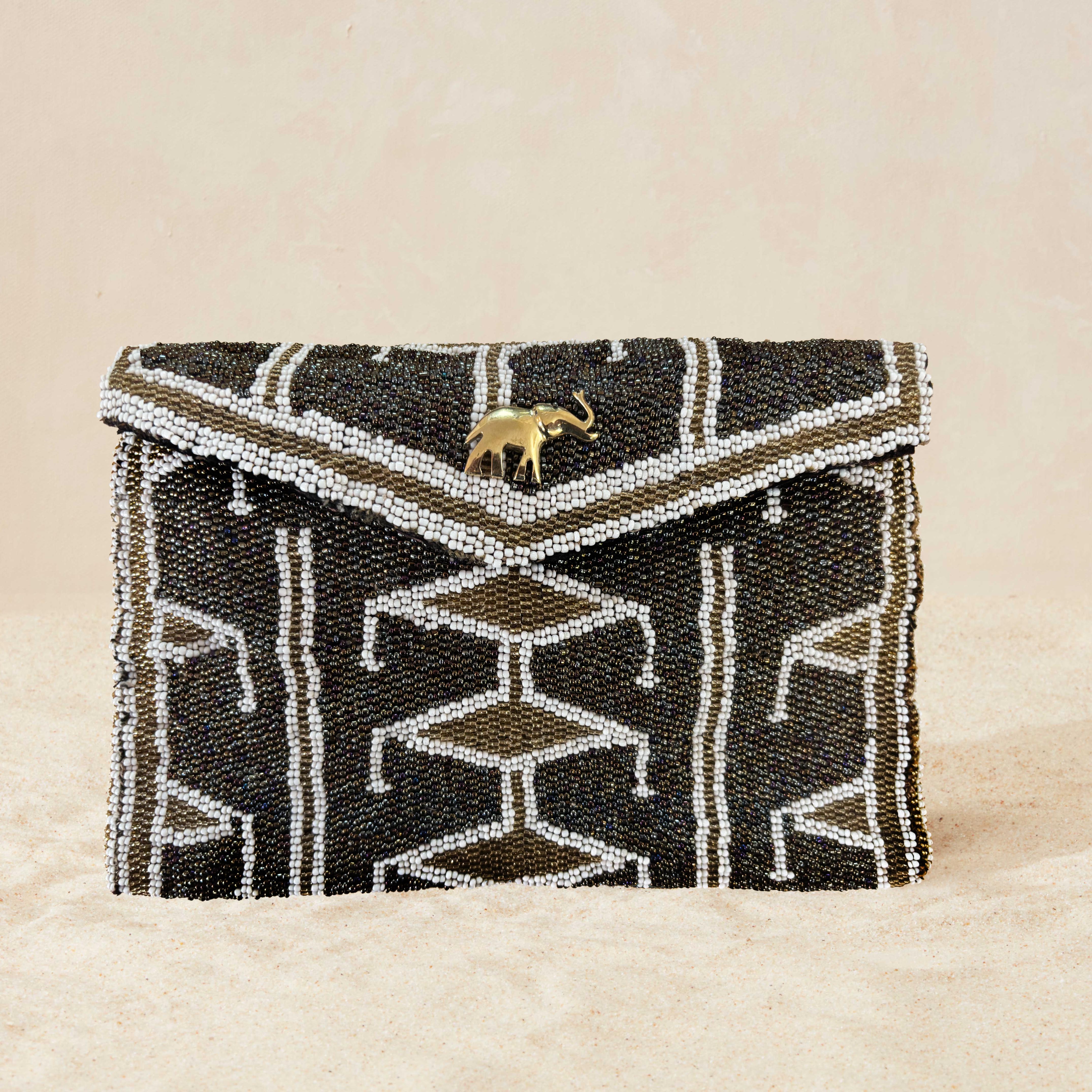 Gold and white beaded clutch with geometric pattern and elephant charm on beige background