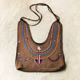 Flat view of brown caramel leather suede handbag with colorful hand beading on a sand background