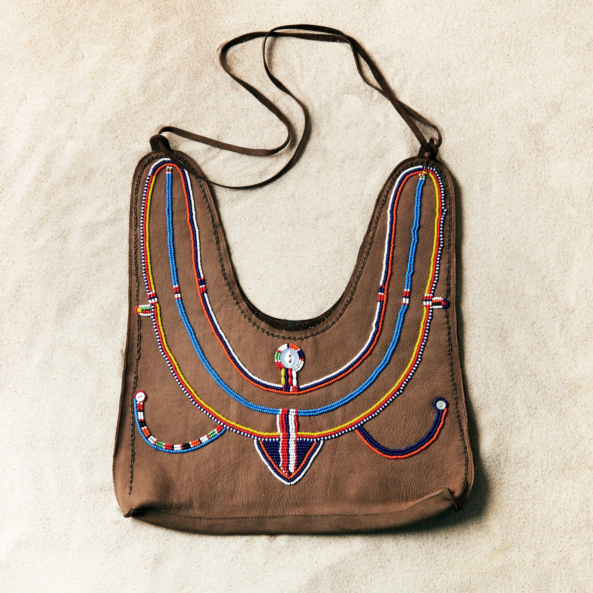 Flat view of brown caramel leather suede handbag with colorful hand beading on a sand background