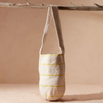 Woven bag with thin yellow stripes hanging on a branch against a beige background