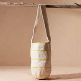 Woven bag with thin yellow stripes hanging on a branch against a beige background