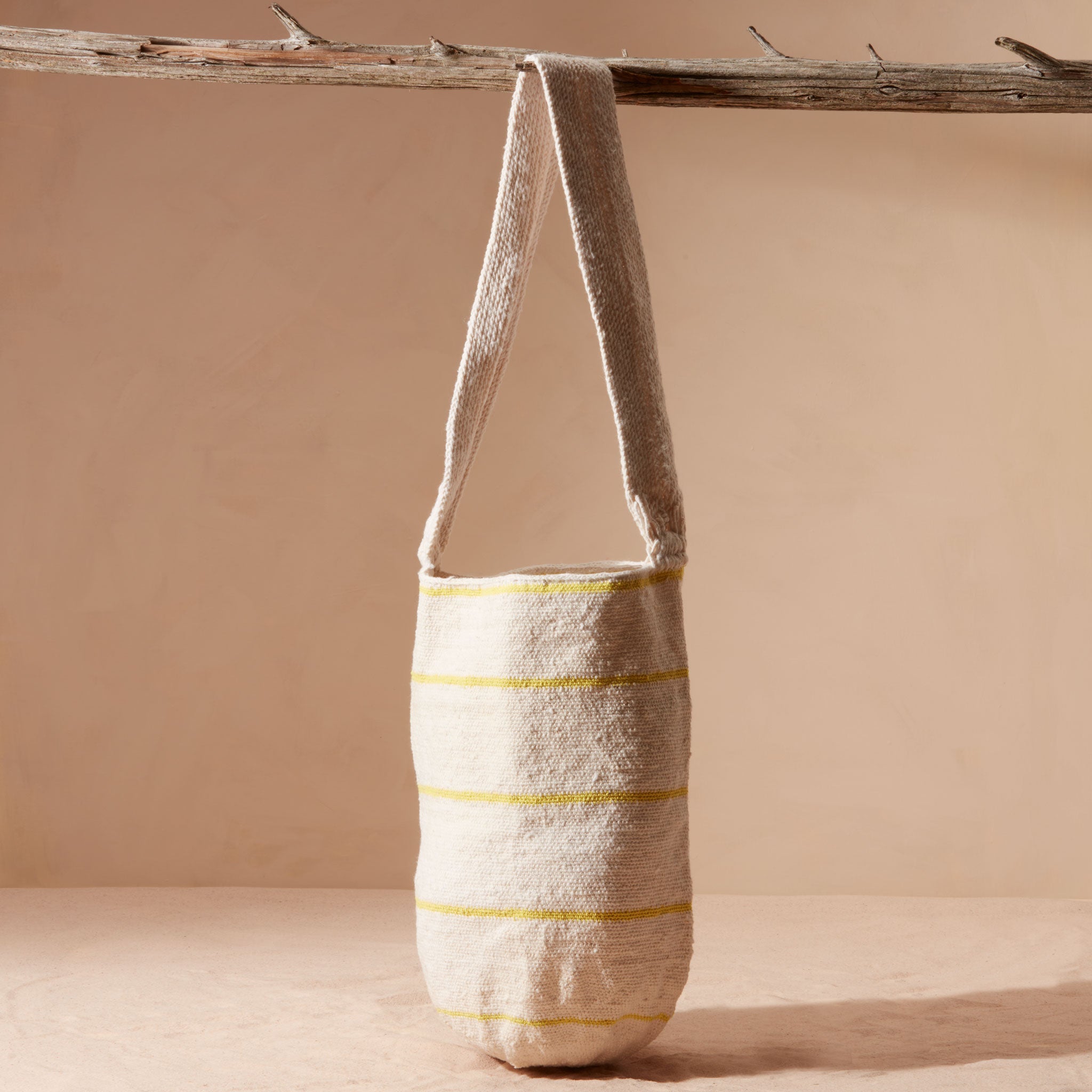 Woven bag with thin yellow stripes hanging on a branch against a beige background