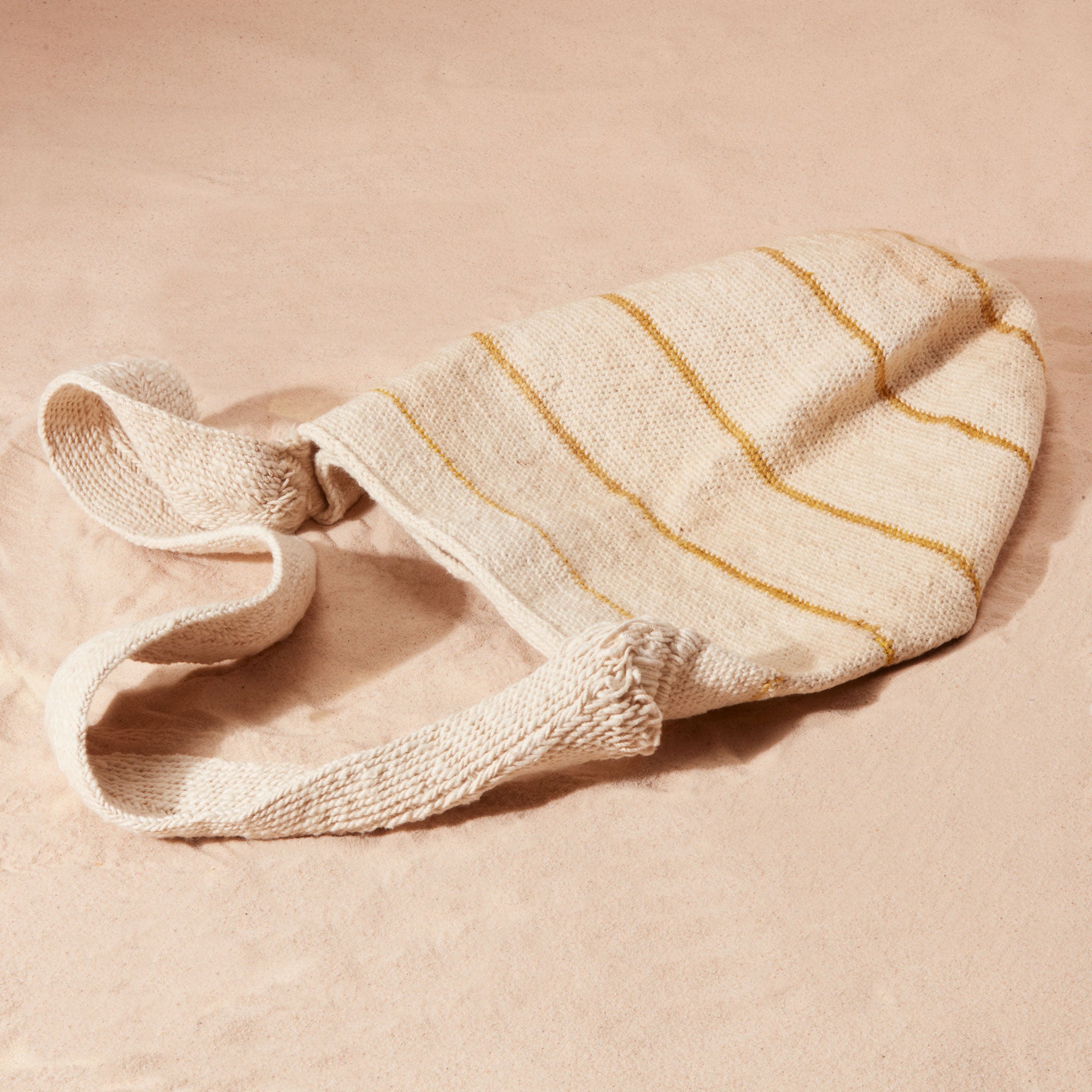 Flat view of Ivory woven bag with yellow/brown stripes on a sand background