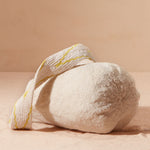 Bottom view of ivory woven bag with yellow and beige v patterned strap on a beige background